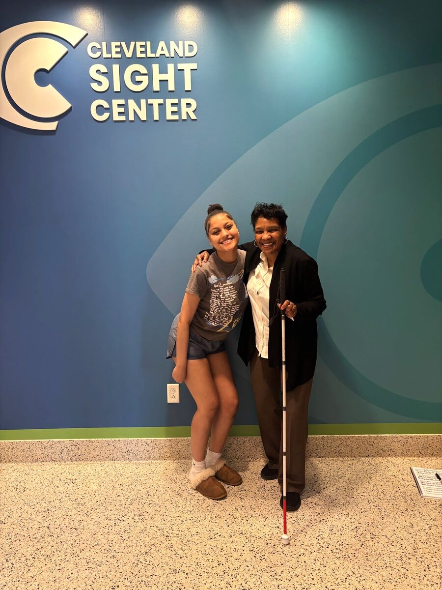 Aaliyah smiles for a photo with a mentor from Cleveland Sight Center. They're standing in front of CSC's branded wall with their logo on it.
