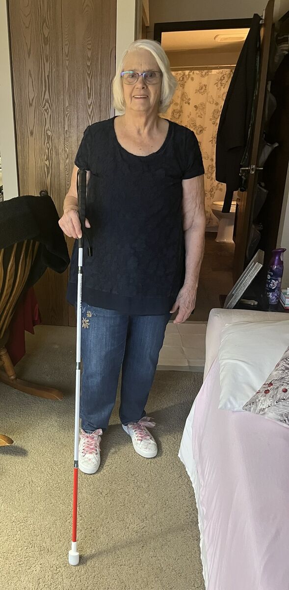 Carrie smiles as she stands for a photo showing off her white cane in her home.