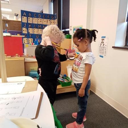 A preschooler pretending to be a doctor holds a stethoscope to listen to his friend's heartbeat.