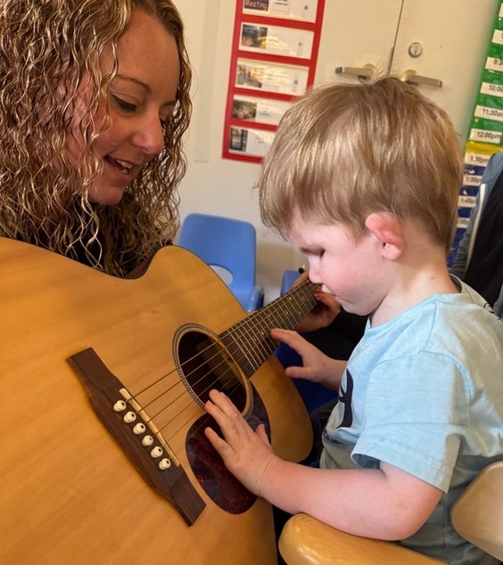 Enoch puts his hands out in front of him to feel a guitar held out to him by musical therapist in CSC's Preschool.