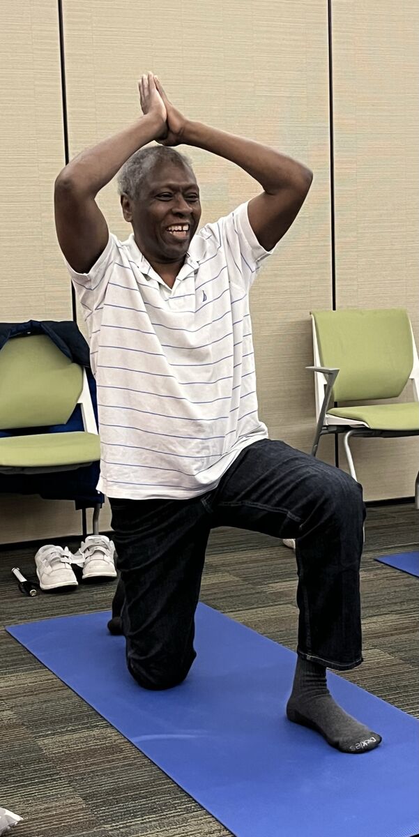 John smiles while doing a lunge pose in yoga class.