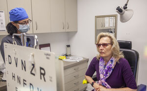 An eye doctor looks at a patient who is reading an eye chart in CSC's clinic.
