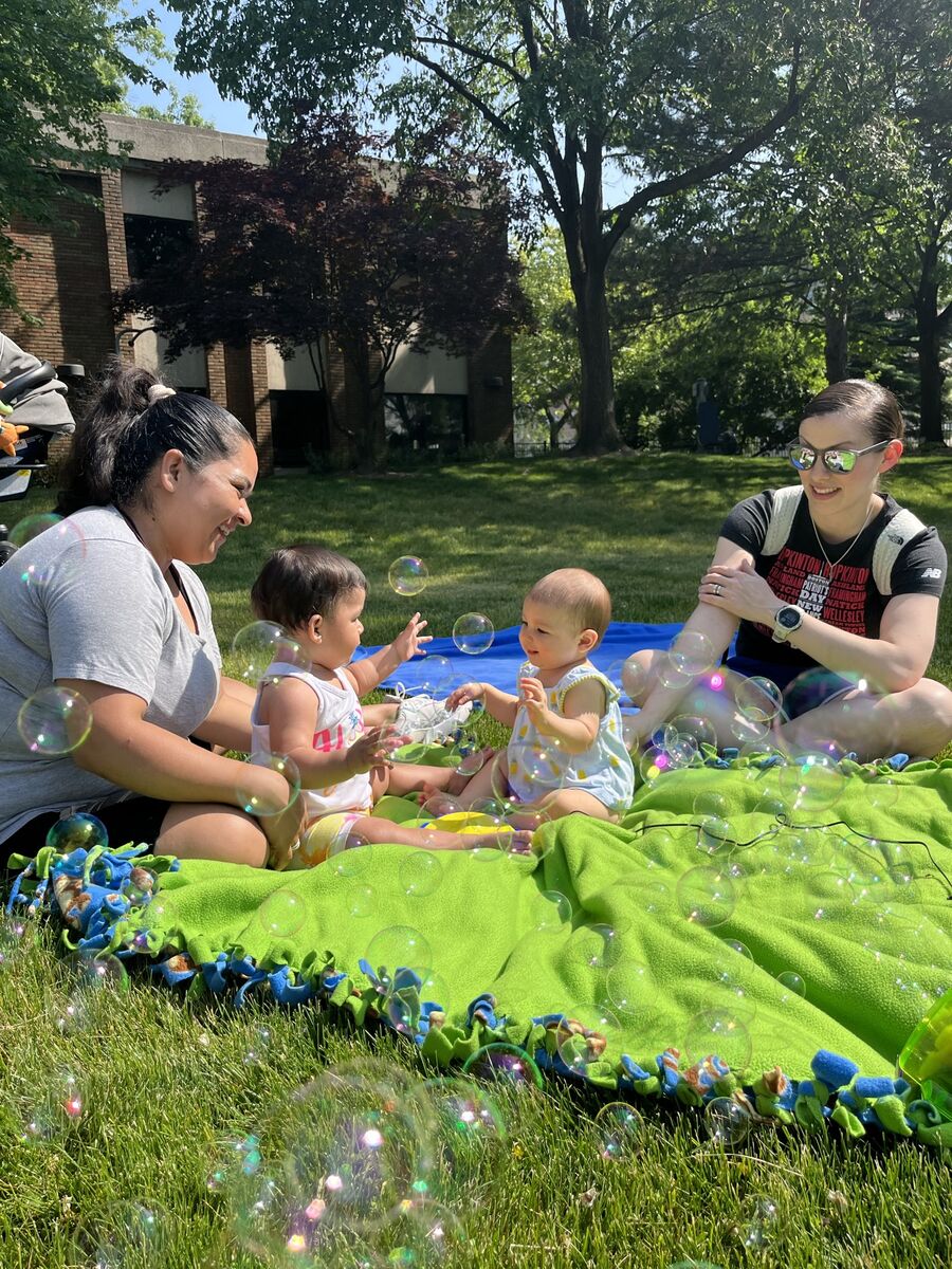 Two early intervention kids play together with bubbles while their mom's watch with smiles on their faces.