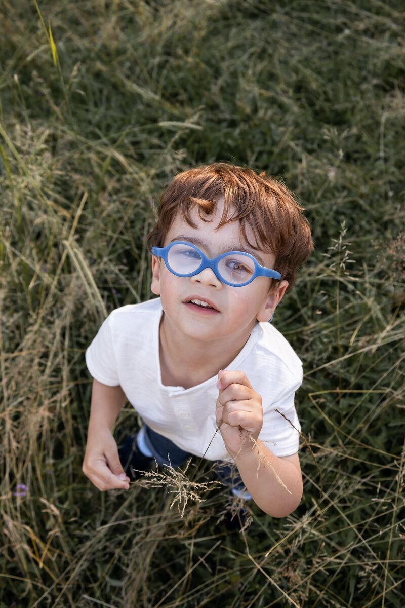 Vincent looks up at the camera, while wearing his blue glasses. He's standing in some tall grass.