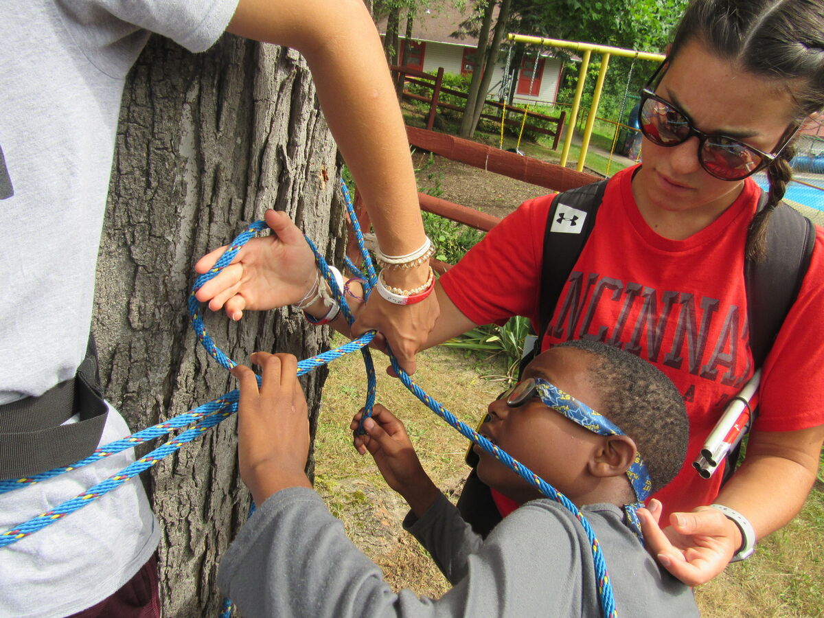 Campers learning to tie knots around a tree