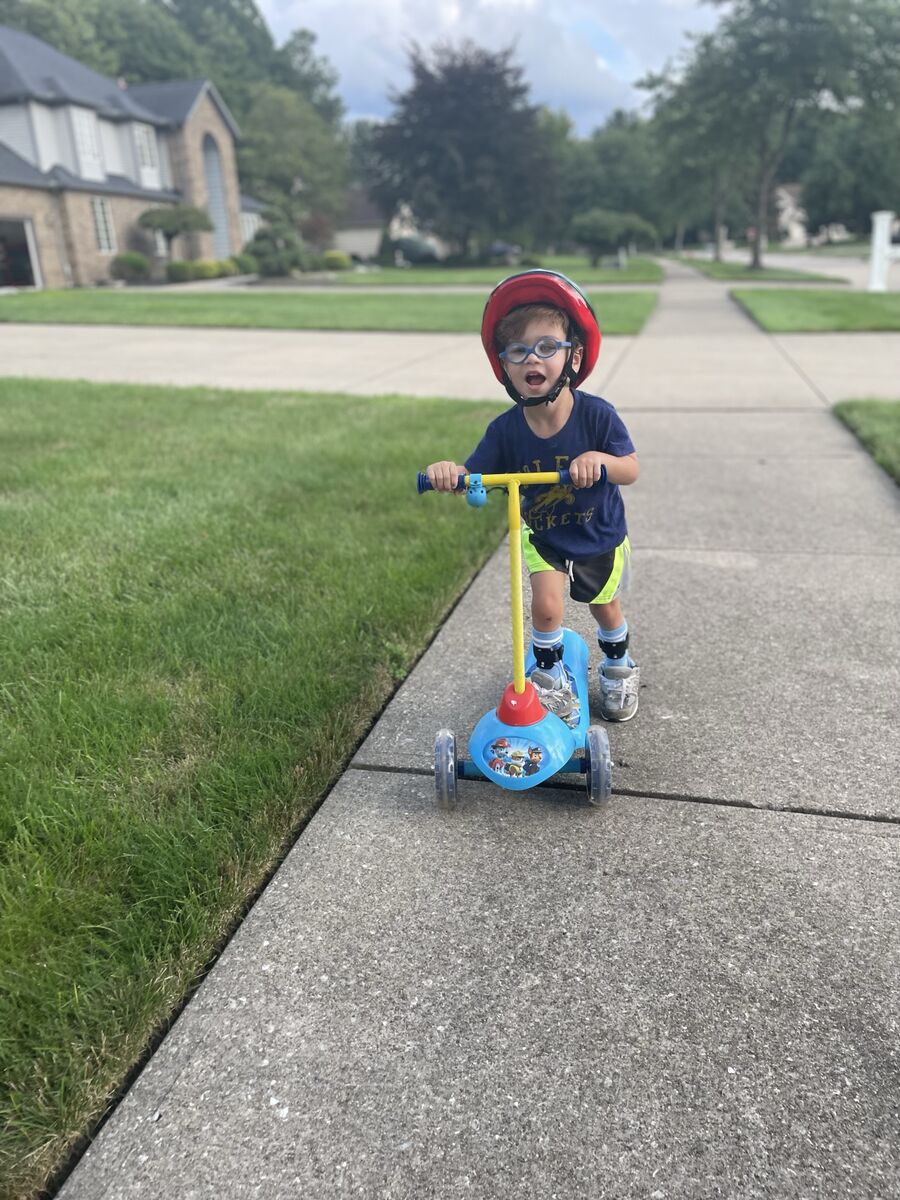 Vincent plays on his scooter on a sidewalk. He's wearing a helmet and has a happy expression on his face.