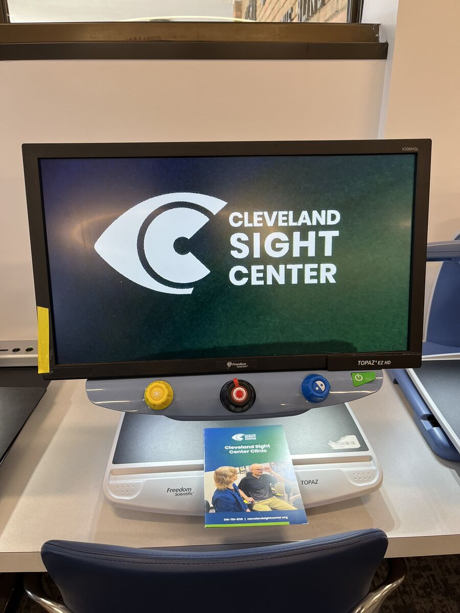 A CCTV has a brochure titled, "Cleveland Sight Center Clinic" resting on its tray, and its display screen is showing the brochure magnified so it's easier to read and see it. The image is so magnified that only the Cleveland Sight Center logo is fits on the screen.