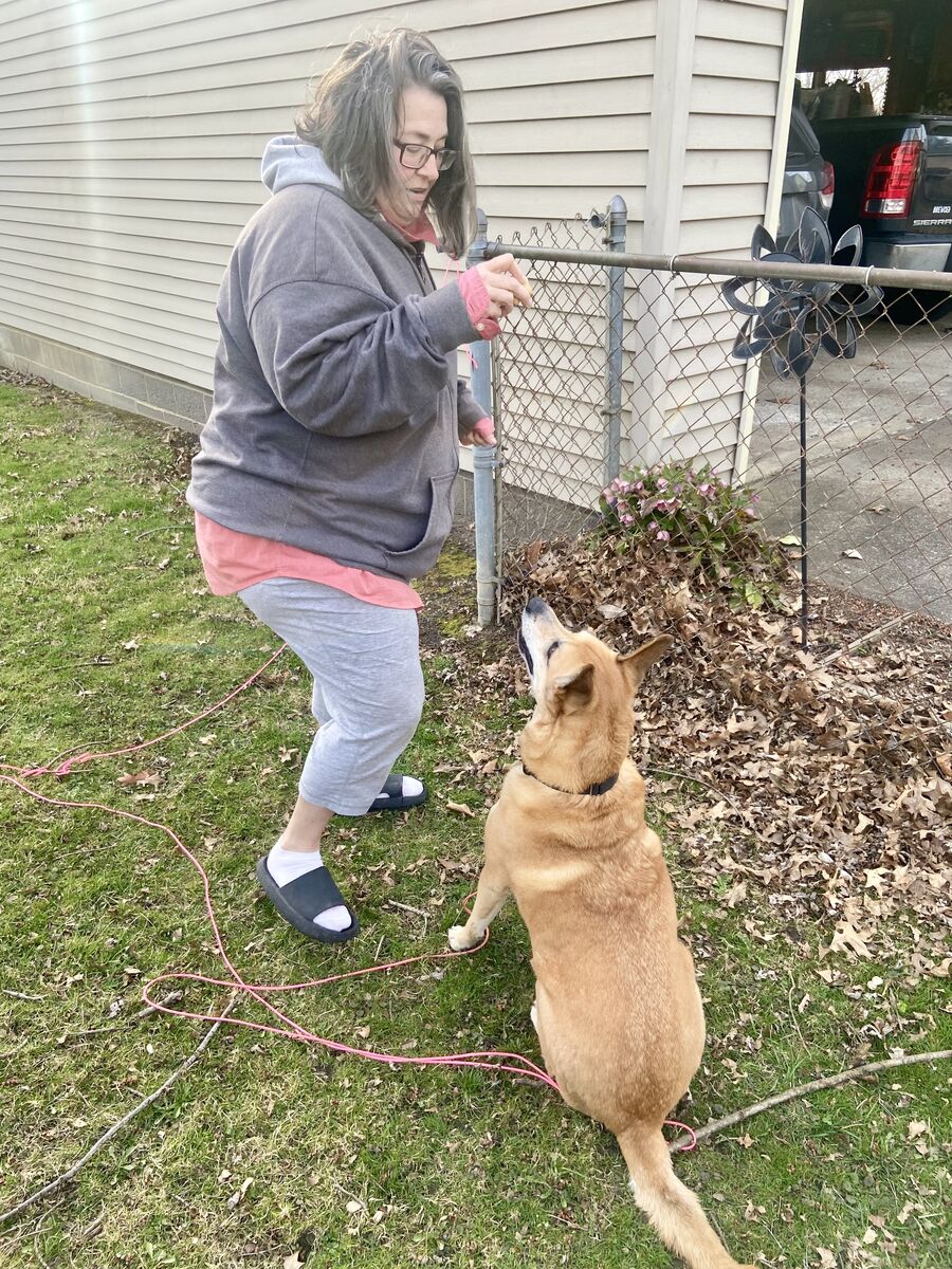 Ruth holds up a treat for her dog, who is sitting on the ground in front of her. 