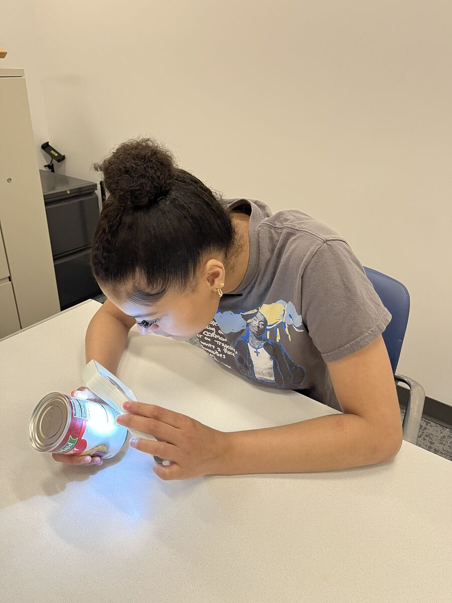 Aaliyah uses a magnifier with a light on it to read the label of a soup can.