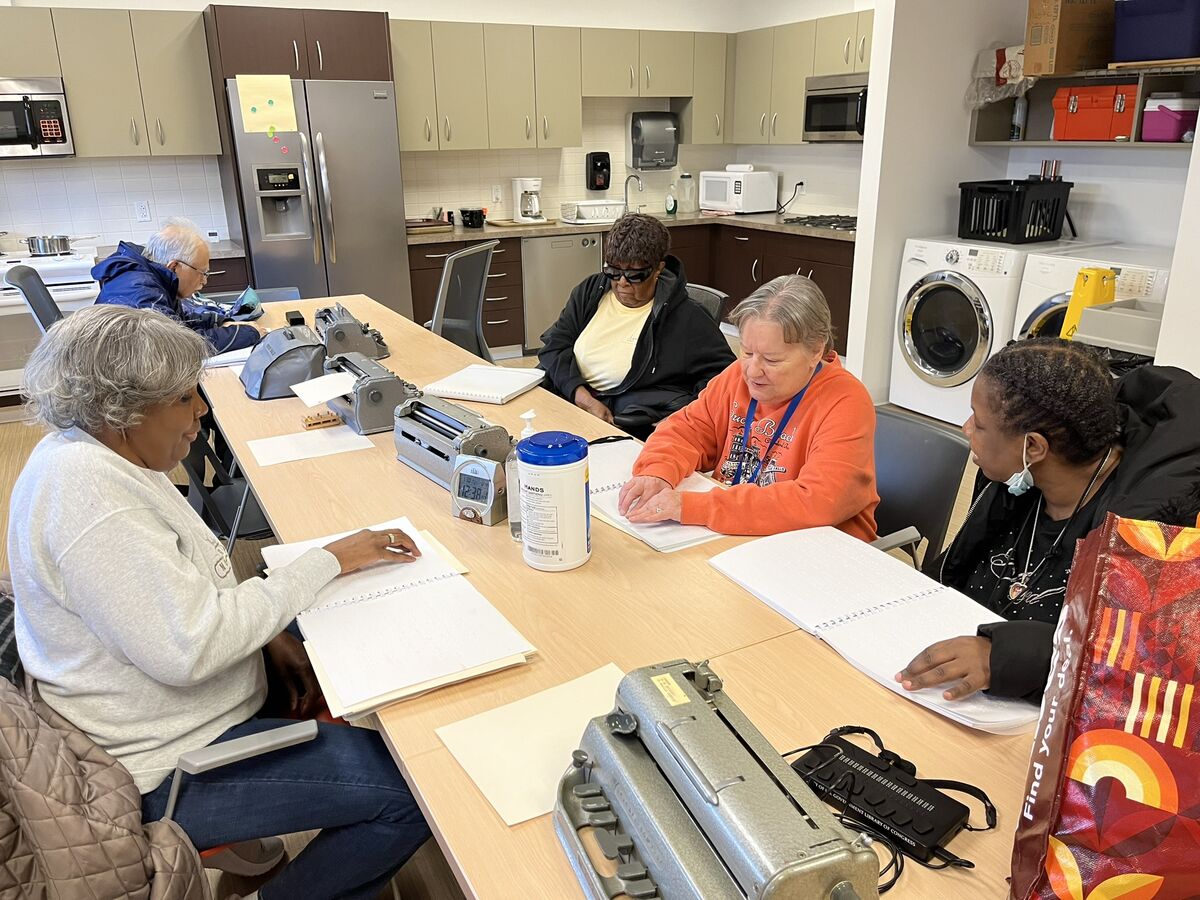 Annette and her four students read from a braille workbook together at a table in CSC's prep kitchen.