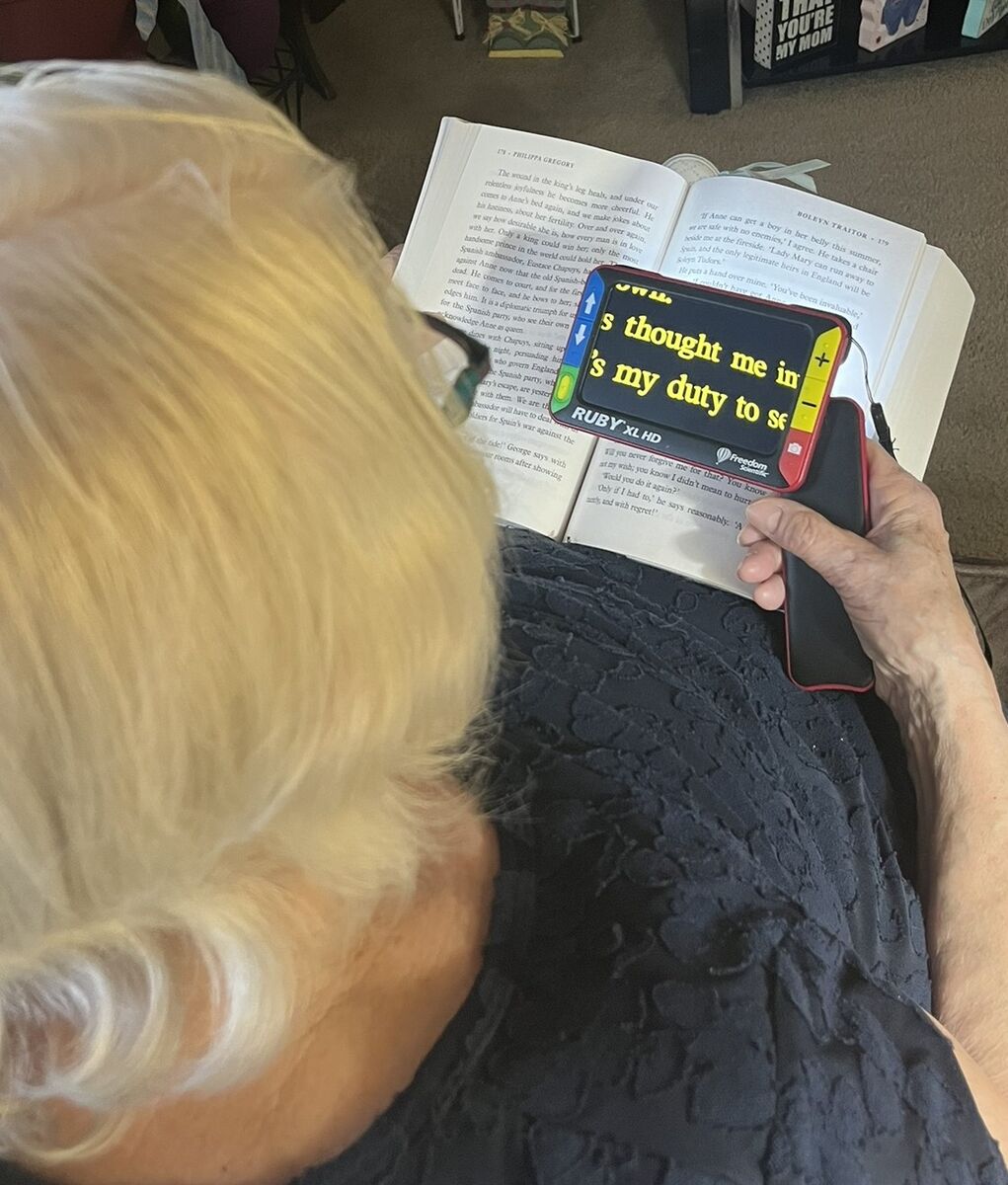 Carrie's magnifier makes the background black and the font white on its screen. The text on the screen is enlarged and from the large book on her lap.