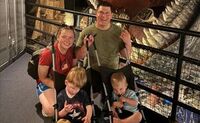 A family photo of Enoch, Nehemiah and their parents smiling together at a museum. Both boys are in strollers.
