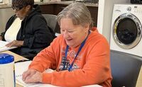 Annette smiles while reading a braille book with her braille class.