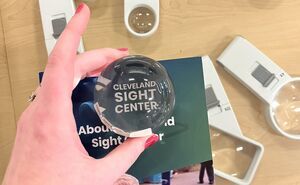 A hand uses a bubble shaped magnifier to read the Cleveland Sight Center logo on a brochure
