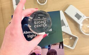 A hand uses a bubble shaped magnifier to read the Cleveland Sight Center logo on a brochure