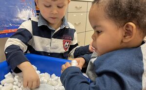 Two preschool boys play in a sensory bin together, touching all the different textures.