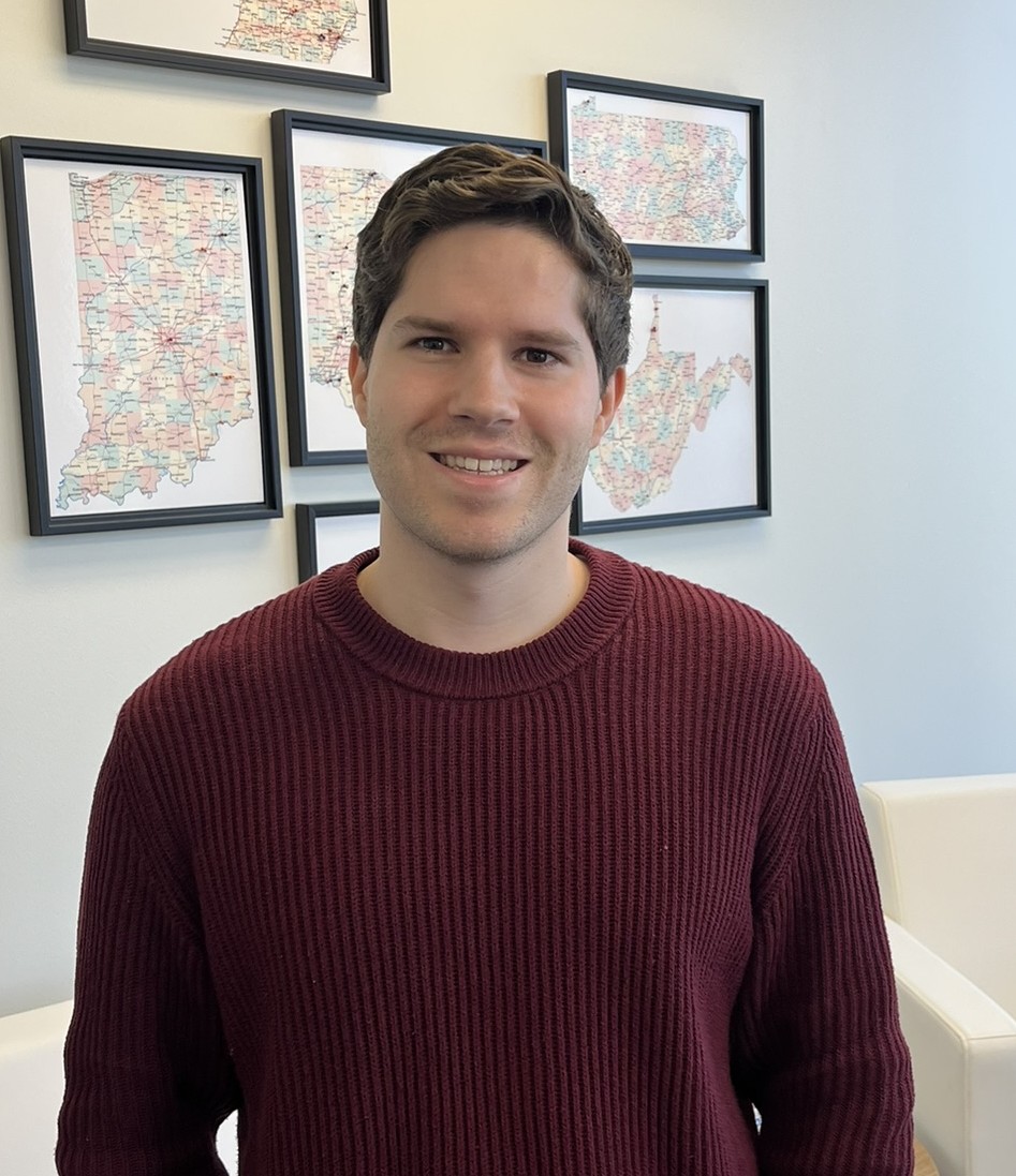 Colin smiles for the camera in a meeting room, with framed maps of states with pins in them.