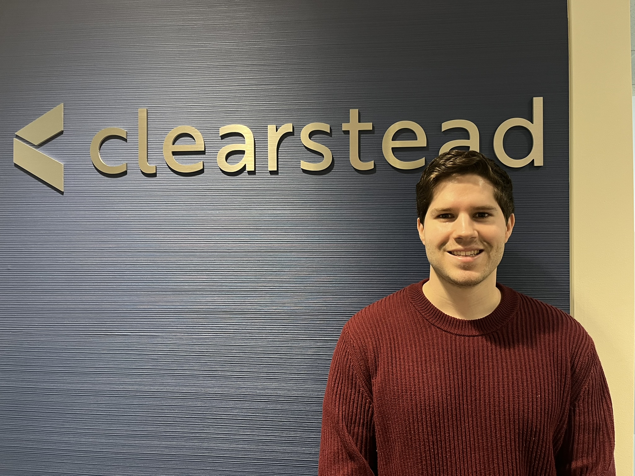 Colin smiles for a photo in front of the Clearstead sign in his office building.