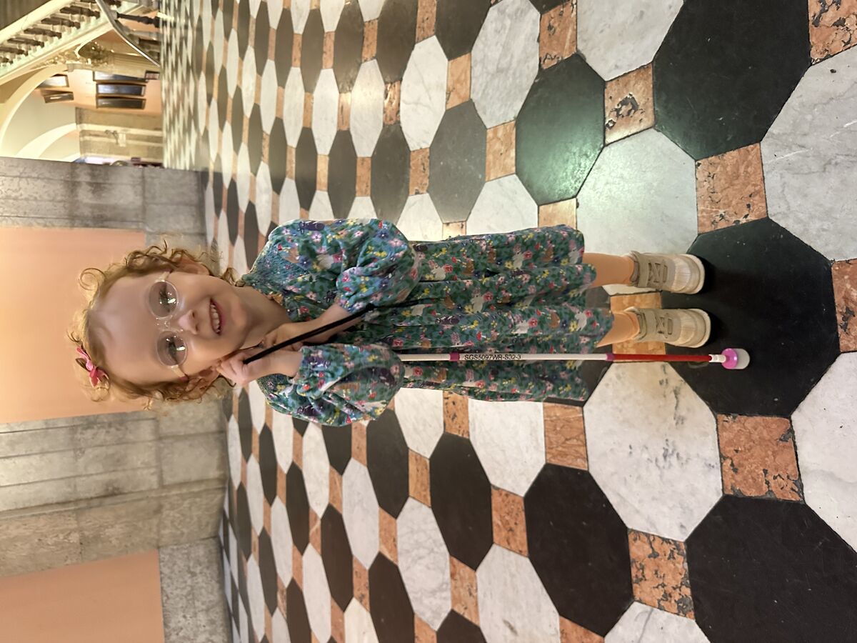 Emma, at 3 years old, poses with her white cane in the Ohio Statehouse rotunda, in a dress.