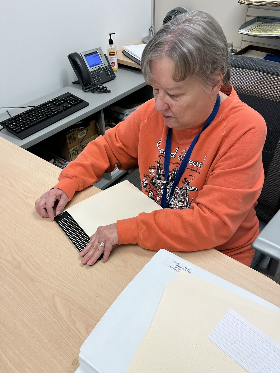 A photo of Annette getting a slate ready to use on a piece of braille paper in her office. 