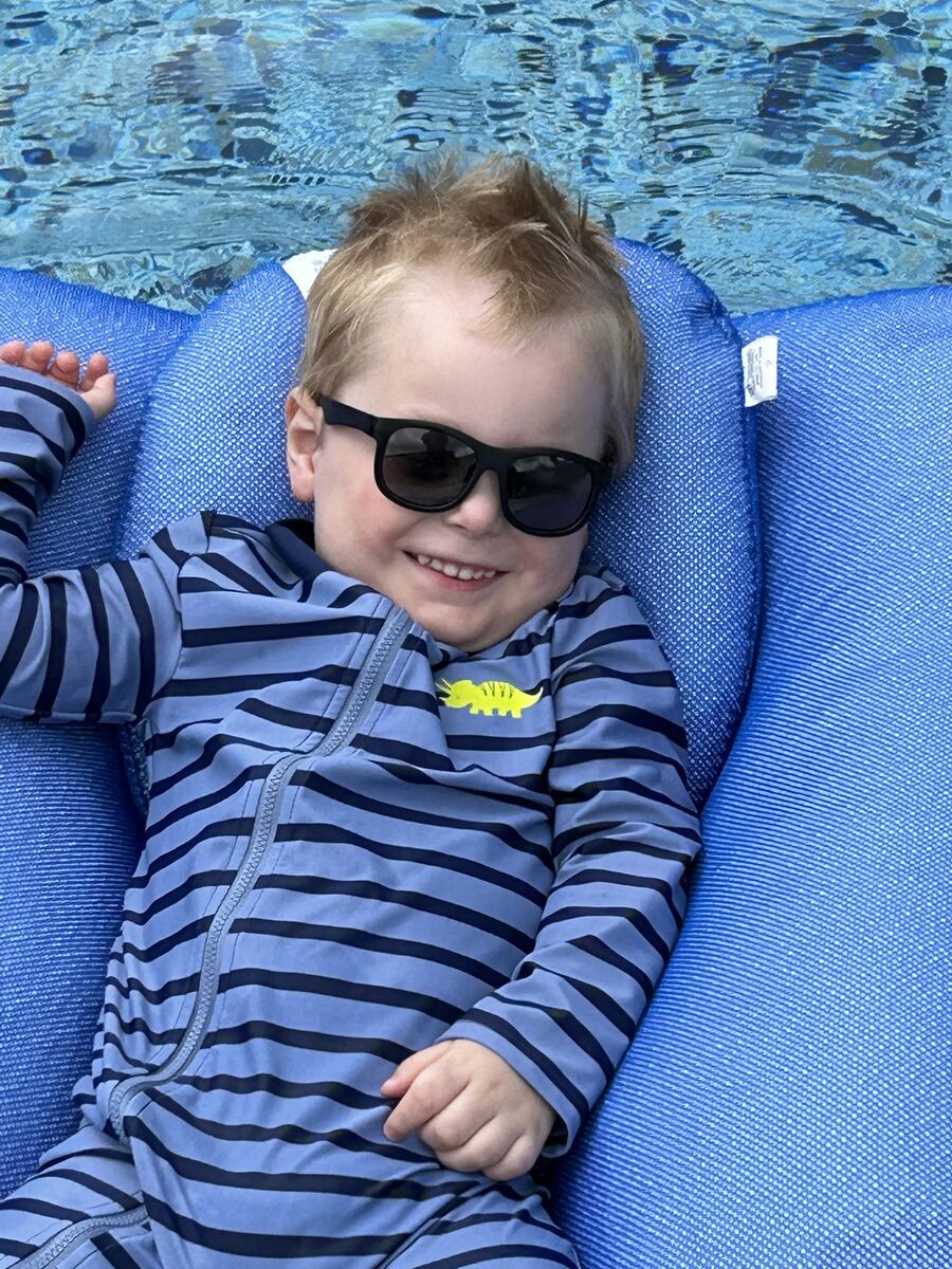 Hayden smiles while laying on a pool floaty and wearing sunglasses.