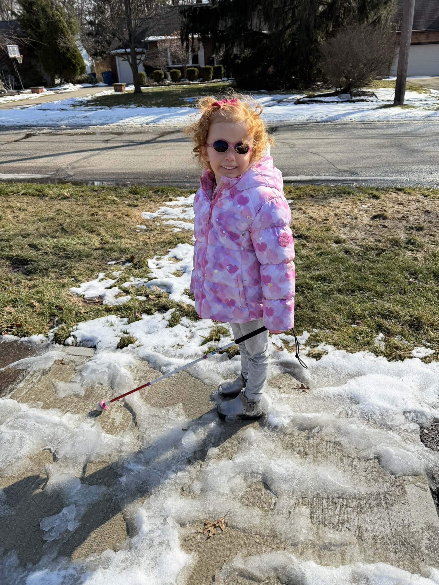 Emma as a 4-year-old, smiling in a winter coat as she uses her white cane to navigate a snowy sidewalk.