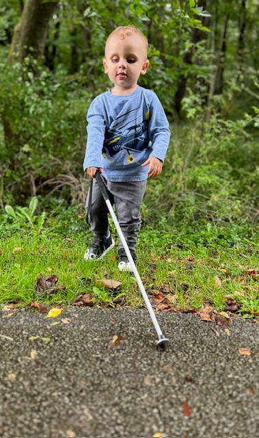 James holds out his white cane as he walks onto a paved trail.