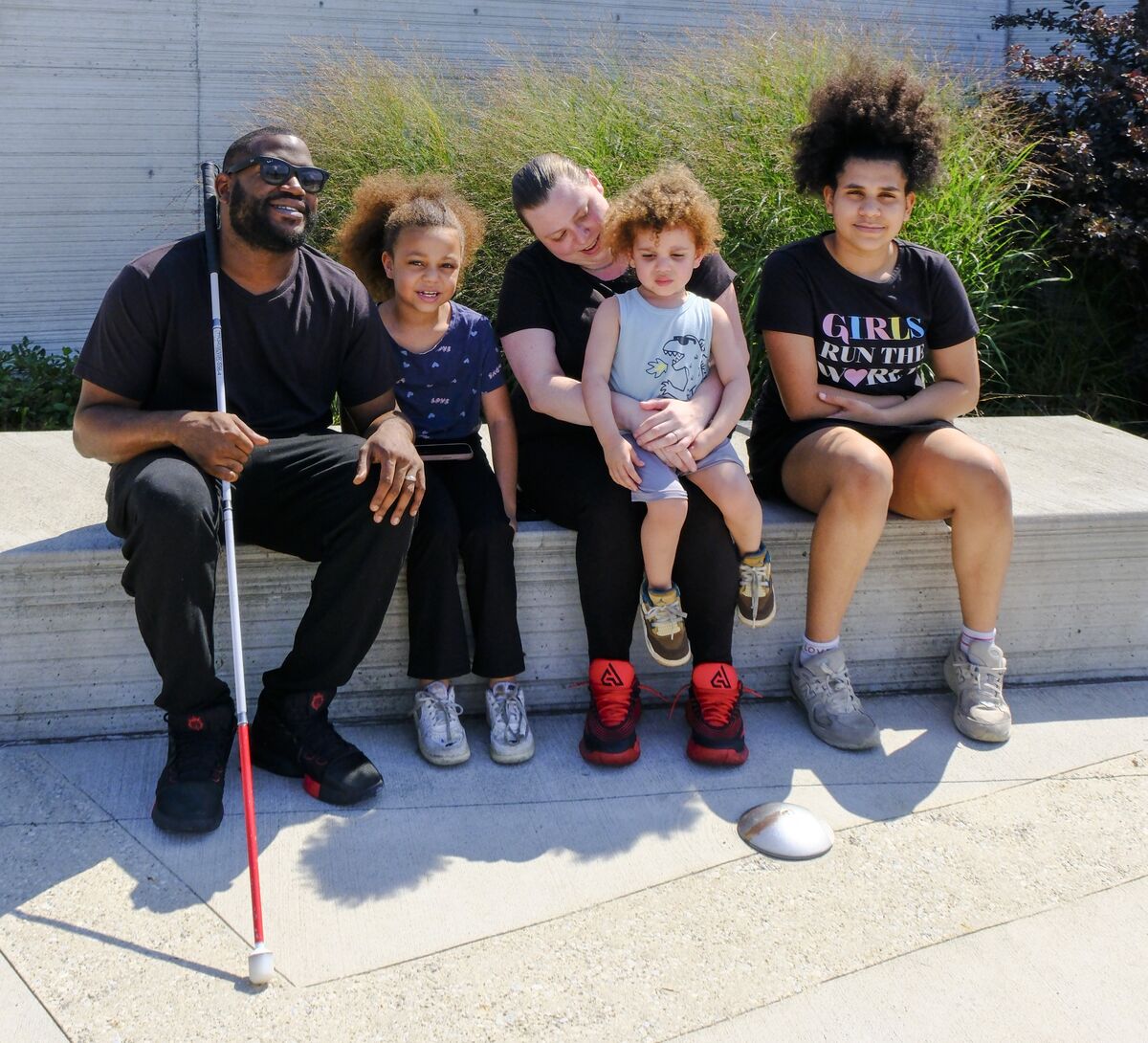 Kayshawn sits with his family on a bench. From left to right is Kayshawn, his second daughter, his wife who is holding their son, the youngest and his eldest daughter.