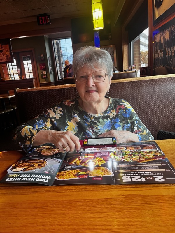 Sandy uses her electronic Ruby magnifier to read a restaurant menu. She's sitting at a table with booth seating.