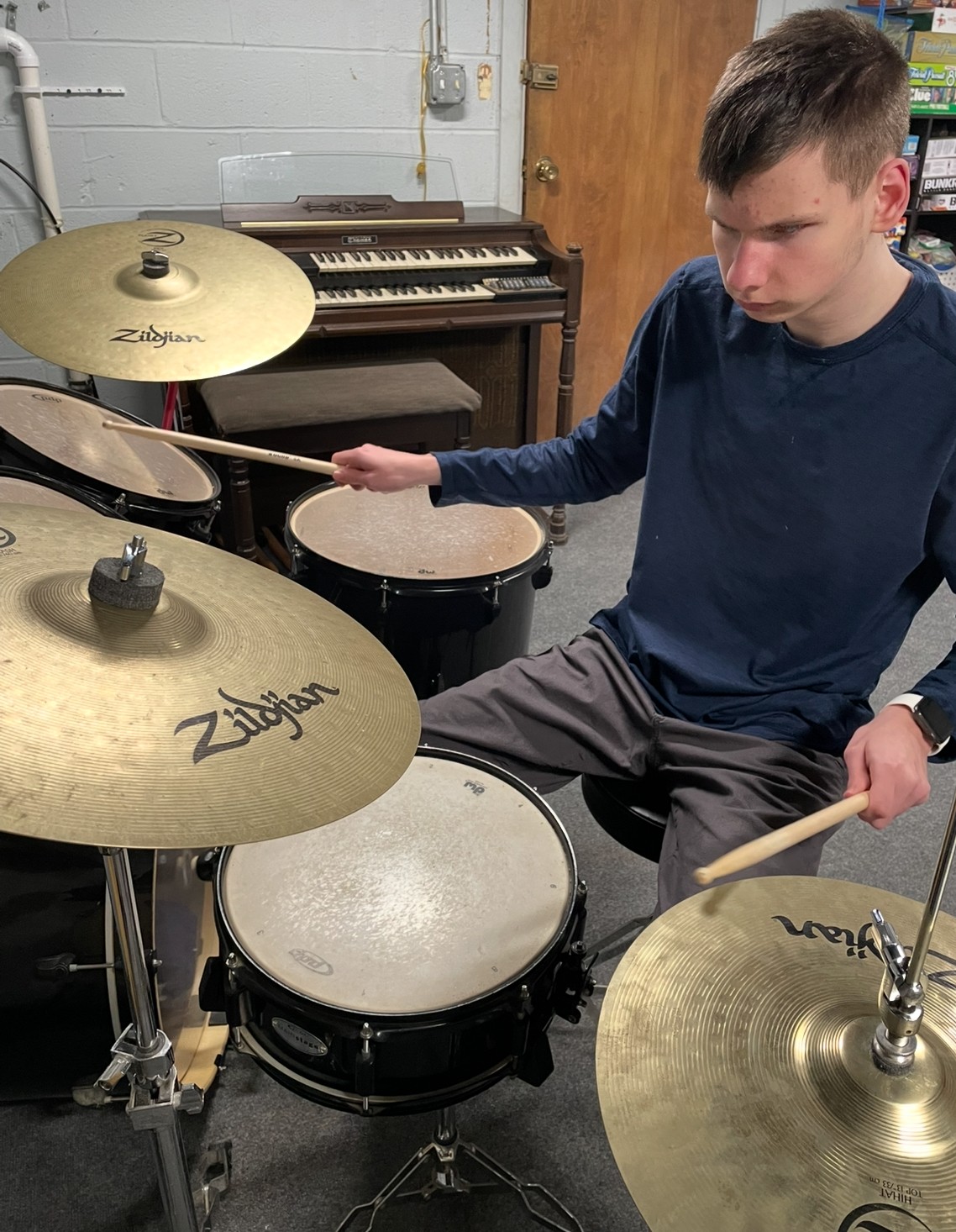 Russell makes a focusing face as he drums on a drumset.