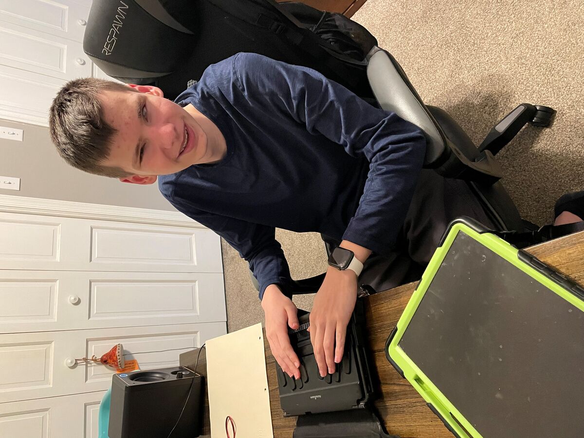 Russell sits at a desk and uses a BrailleNote Touch Plus. He's smiling at the camera!