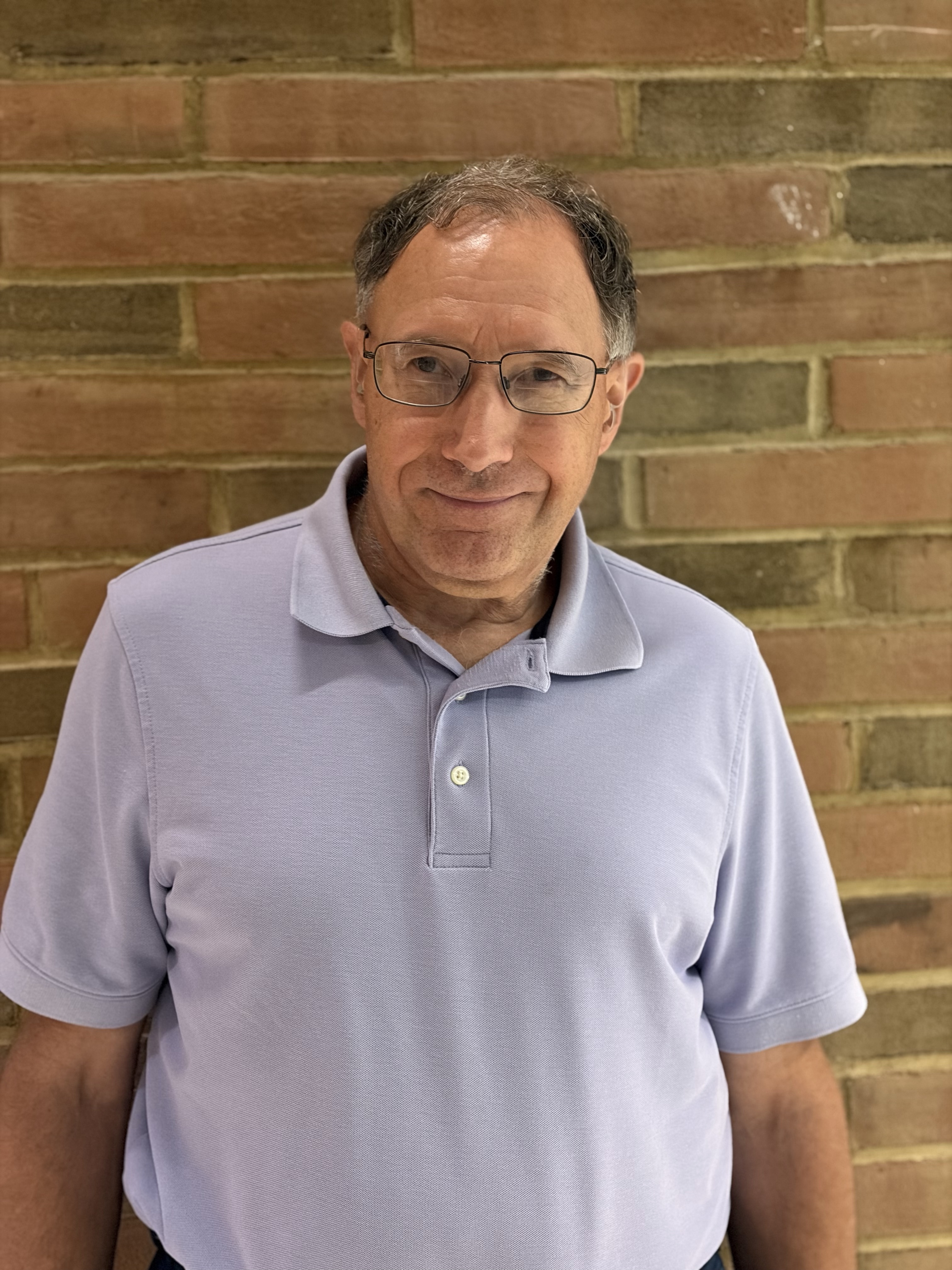 Tom smiles for a photo in front of a brick wall