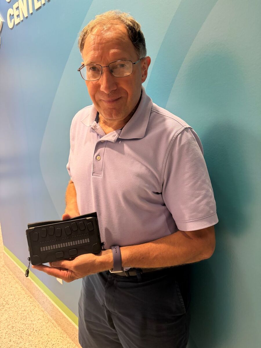 Tom smiles as he holds up a braille note display