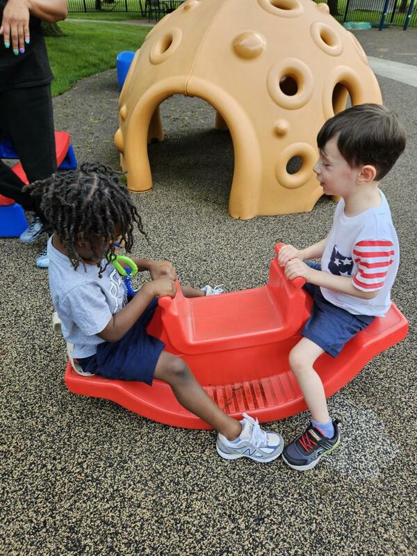 Two preschoolers sit on a teeter totter toy together on CSC's playground.