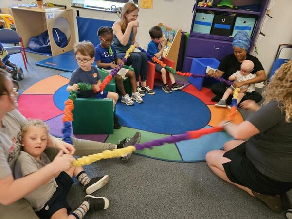 A group of preschool students sit with their teachers and aid for a musical therapy activity.