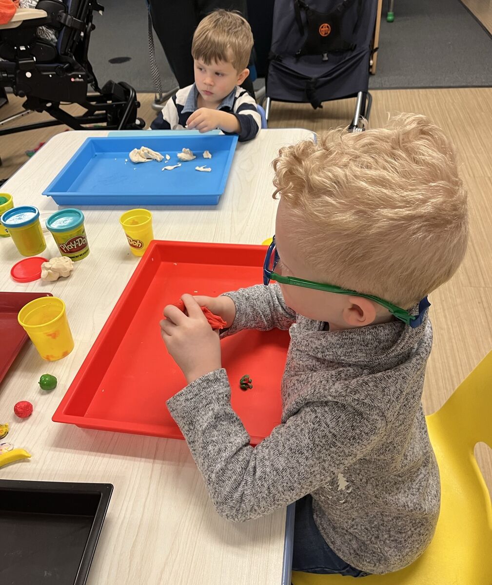 Two preschoolers sit at a table and look through playdough to find surprises inside 