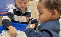 Two preschool-aged boys play in a sensory bin and feel the different textures inside.