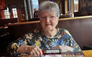 Sandy smiles at the camera while using her ruby magnifier to read a restaurant menu